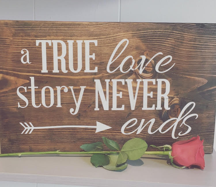 Wood board with the quote a true love story never ends painted on it